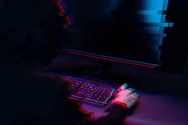 Kapüşonlu hacker karanlık odada bilgisayar yazma metni ile çalışıyor. Glitch efektli görüntü