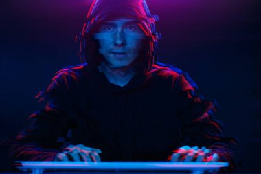 Kapüşonlu hacker karanlık odada bilgisayar yazma metni ile çalışıyor. Glitch efektli görüntü