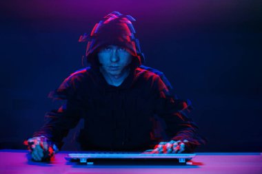 Kapüşonlu hacker karanlık odada bilgisayar yazma metni ile çalışıyor. Glitch efektli görüntü