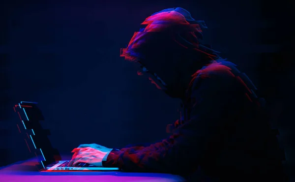 Hacker karanlıkta metin yazarak dizüstü bilgisayar ile çalışıyor kaputta. Glitch efektli görüntü