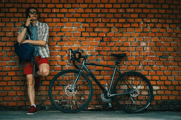 Um jovem homem elegante posando ao lado de sua bicicleta . — Fotografia de Stock