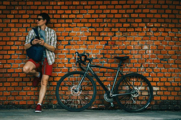 Um jovem homem elegante posando ao lado de sua bicicleta . — Fotografia de Stock