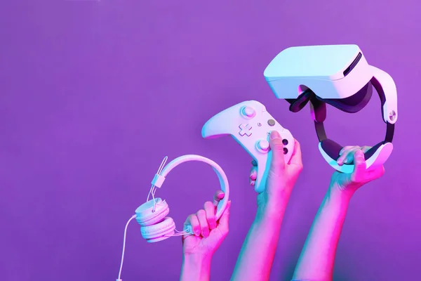 Uppsättning händer med gamepad, Virtual Reality headset och hörlurar på violett bakgrund. — Stockfoto