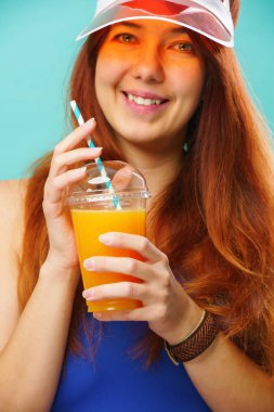 Mavi mayo giyen ve şapka içen kadın bir bardaktan meyve suyu içiyor