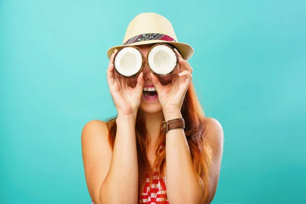Mujer con un traje de baño y sombrero de paja sosteniendo dos partes de coco cerca de sus ojos — Foto de Stock