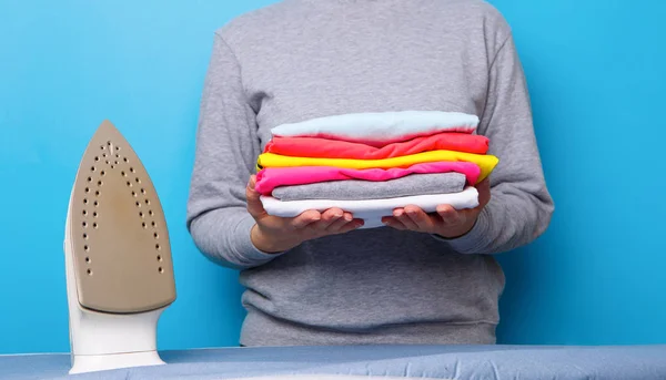 Women with electric iron and pile of clothes in her hands. — Stock Photo, Image