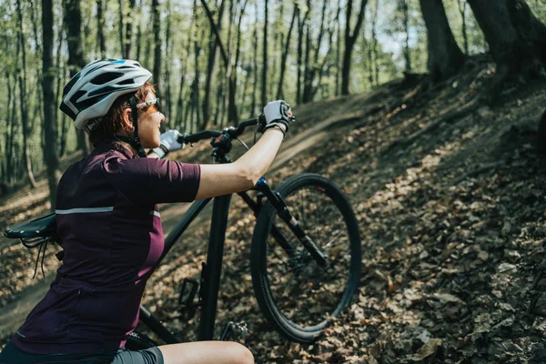 Zdjęcie sportowiec Kobieta w kask podnoszenia rower na wzgórzu w lesie — Zdjęcie stockowe