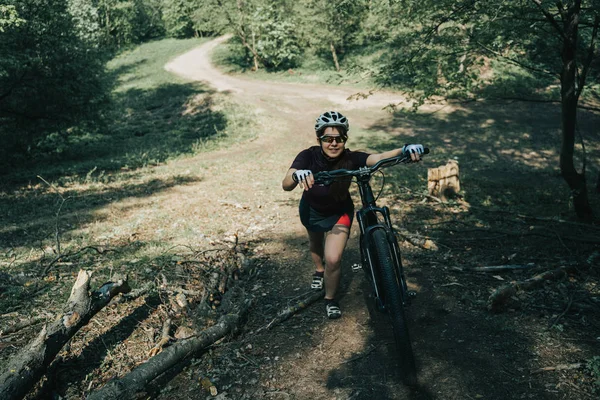 Photo of sportswoman in helmet raising bicycle to hill in forest — Stock Photo, Image