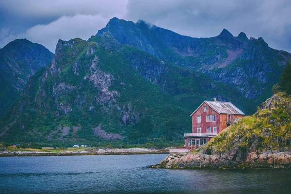 Obrázek červeného domu na úpatí kopců, moře, oblačno nebe, stromy v Norsku — Stock fotografie