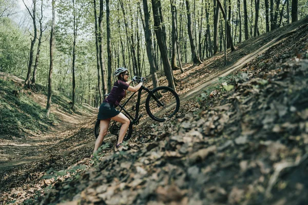 Foto de una atleta en casco elevando bicicleta a colina en el bosque —  Fotos de Stock