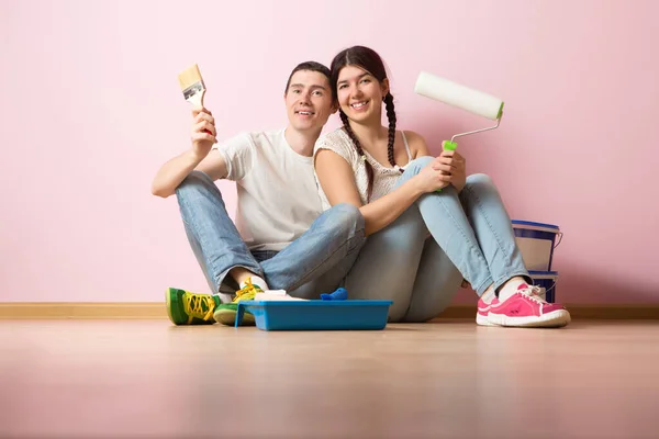 Hombre con pincel y mujer con rodillo de pintura sentado en el suelo — Foto de Stock