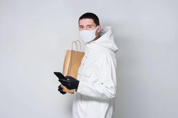 Hombre con una máscara protectora para evitar la propagación de Coronavirus bolsa de la compra y se comunica a través de un teléfono inteligente . —  Fotos de Stock