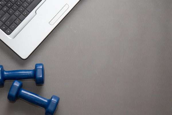 Two dumbbells for fitness at home and a laptop for remote training.