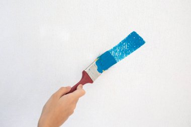 Çocuğun eli, fırça darbesiyle mavi bir boyayla beyaz bir duvar boyuyor.