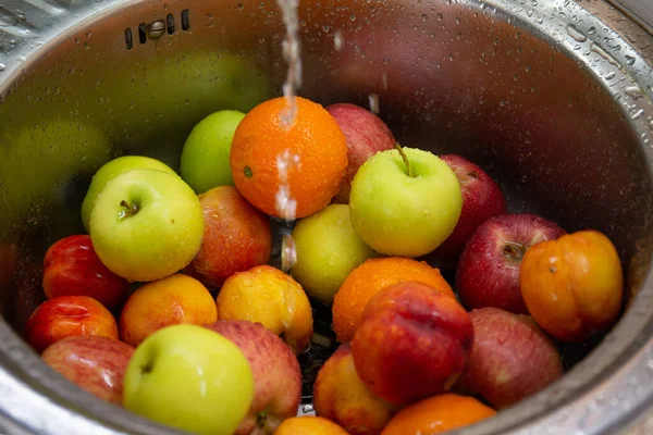 Banyak buah-buahan berwarna yang berbeda: jeruk, apel, nektarin di wastafel dapur di bawah air yang mengalir Stok Lukisan  