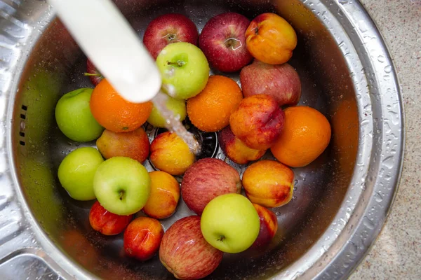 Banyak buah-buahan berwarna yang berbeda: jeruk, apel, nektarin di wastafel dapur di bawah air yang mengalir Stok Foto Bebas Royalti