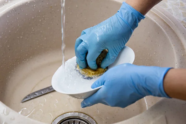 Tangan wanita dengan sarung tangan biru mencuci piring dan piring di wastafel dapur. Konsep rumah tangga — Stok Foto