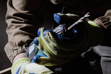 Sarı ve mavi eldiven ve siyah arka plan üzerine bir elektrikli matkap tutan kıyafeti bir closeup marangoz işçi fotoğrafı.
