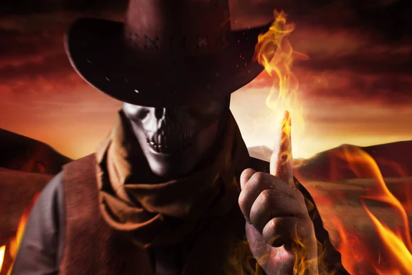 彼の腕と夕日砂漠を背景に指帽子鋳造火の呪文で悪魔のようなスカル ヘッド カウボーイの写真 — ストック写真
