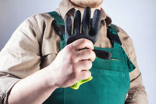 Pracovník v zeleném celkovém oděvu drží rukavici. — Stock fotografie