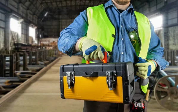 Trabajador con camisa vaquera y chaqueta verde sosteniendo caja de herramientas . — Foto de Stock