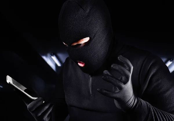 Ladrón macho enojado en máscara y guantes sosteniendo teléfono inteligente . —  Fotos de Stock