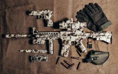 Üzerinde bıçak, silah ve taktik eldivenler bulunan kamufle edilmiş AR-15 tüfeği..
