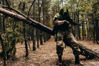 Tam teçhizatlı bir orman keskin nişancısının ormanda duran tüfekli fotoğrafı..