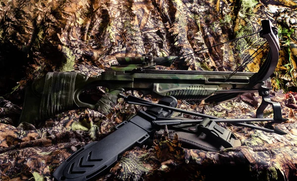 森のカモフラージュテーブルの上に置かれたナイフと矢を持つ狩猟のクロスボウの写真背景 — ストック写真