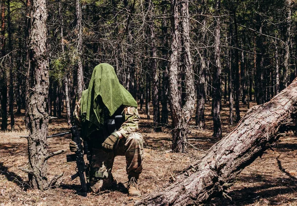 森の中に座ってライフルと戦術的なネットスカーフで完全に装備されたカモフラージュの森の狙撃手の写真 — ストック写真