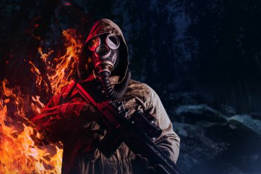 Gaz maskeli, kapüşonlu ceketli, elinde tüfekle karanlık bir orman geçmişinde dikilip yanan kıyamet sonrası takipçi bir askerin fotoğrafı..