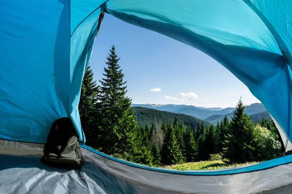 照片上是一个阳光灿烂的日子 从蓝色露营帐篷门到旅行背包的山林景观 — 图库照片