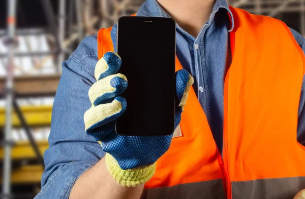 Foto Trabalhador Masculino Uniforme Jaqueta Laranja Luvas Segurando Smartphone Preto — Fotografia de Stock
