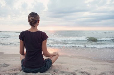 Dışarıda yoga yapan genç bir kadın. Arka planda gün batımı manzaralı meditasyon yapan bir kız. Uyum, meditasyon, rahatlama, tatiller, özgürlük, sağlıklı yaşam tarzı konsepti