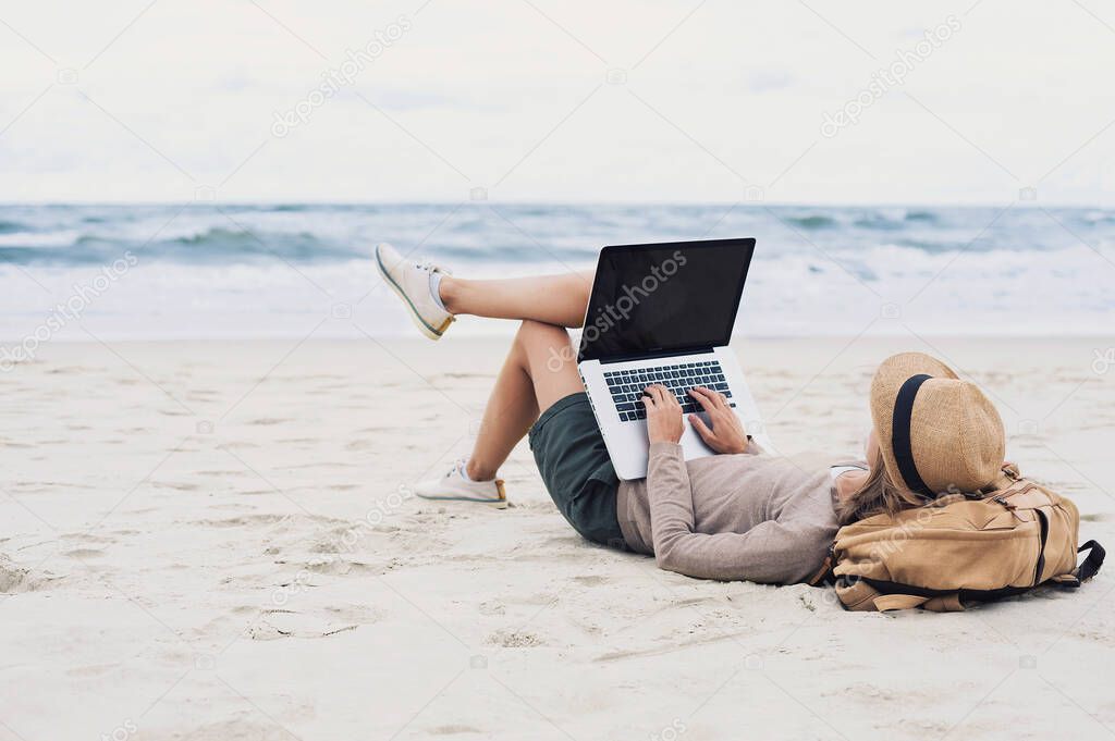 Young woman using laptop on a beach, blank empty screen monitor, Freelance work, technology, distance education, studying, vacations, travel concept