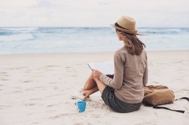Kumsalda kitap okuyan genç bir kadın. Dinlenme dinlenme tatili kavramı