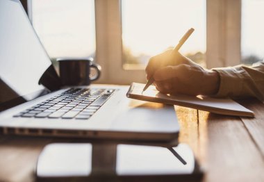 Genç adam çalışıyor, dizüstü bilgisayar kullanıyor ve not defterine yazıyor.