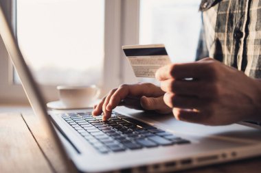 Kredi kartı tutan ve evde dizüstü bilgisayar kullanan bir adam, bilgisayar, online alışveriş, e-ticaret, internet bankacılığı, harcama para konsepti üzerinde çalışan bir iş adamı veya girişimci.
