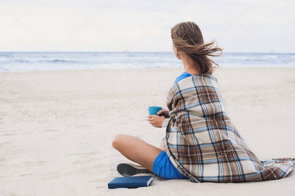 Young woman sitting on beach and looking at the sea. Relaxation concept