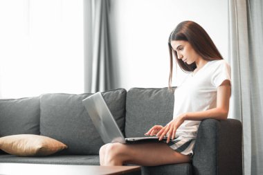 Modern dizüstü bilgisayarı olan genç bir kadın evdeki kanepede oturuyor. Boş zamanlarında internette gezinen mutlu kız... 