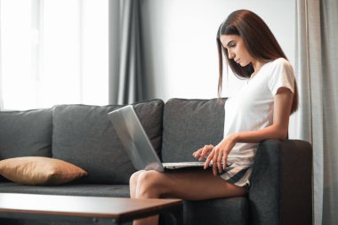 Modern dizüstü bilgisayarı olan genç bir kadın evdeki kanepede oturuyor. Boş zamanlarında internette gezinen mutlu kız... 