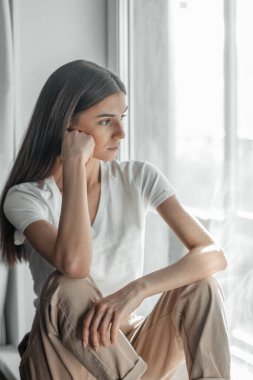 Pencerenin arkasındaki güzel genç kadın portresi. Çekici Kafkas model kız. Yumuşak güneş ışığı. Gün doğumu ya da gün batımı.