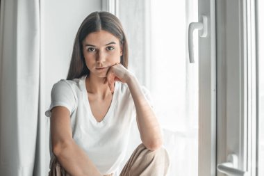 Pencerenin arkasındaki güzel genç kadın portresi. Çekici Kafkas model kız. Yumuşak güneş ışığı. Gün doğumu ya da gün batımı.