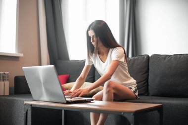 Modern dizüstü bilgisayarı olan genç bir kadın evdeki kanepede oturuyor. Boş zamanlarında internette gezinen mutlu kız... 