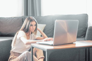 Modern dizüstü bilgisayarı olan genç bir kadın evdeki kanepede oturuyor. Boş zamanlarında internette gezinen mutlu kız... 