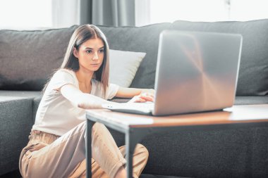 Modern dizüstü bilgisayarı olan genç bir kadın evdeki kanepede oturuyor. Boş zamanlarında internette gezinen mutlu kız... 