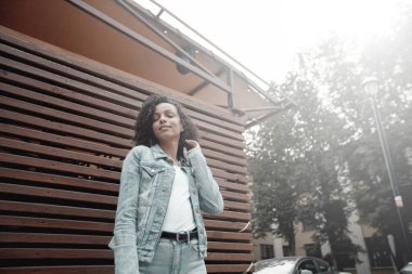 Siyah, genç ve güzel bir kız dışarıda dinleniyor. Sokak hipster portresi. Yürüyen öğrenci kadın.