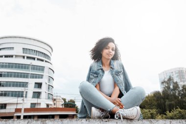 Siyah, genç ve güzel bir kız dışarıda dinleniyor. Sokak hipster portresi. Yürüyen öğrenci kadın.