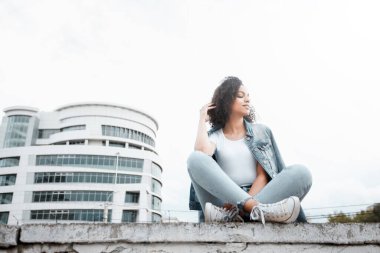 Siyah, genç ve güzel bir kız dışarıda dinleniyor. Sokak hipster portresi. Yürüyen öğrenci kadın.