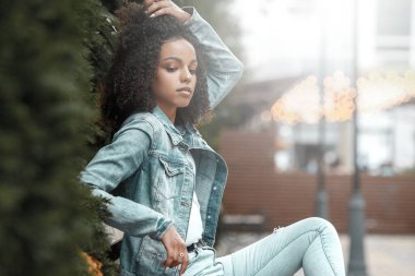 Caddedeki siyah kıvırcık kız. Güneşli yaz şehri. Genç kadın kot tarzı.